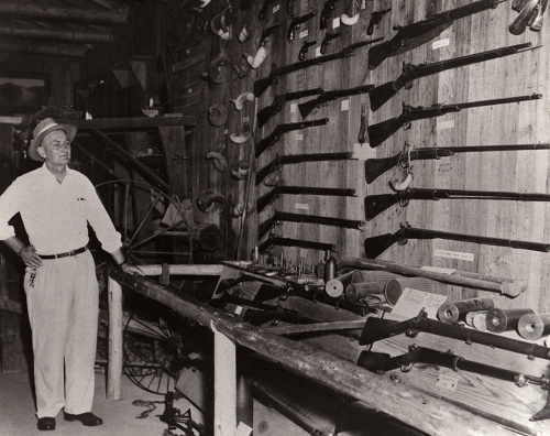 John B. Battle standing next to his collection of guns.